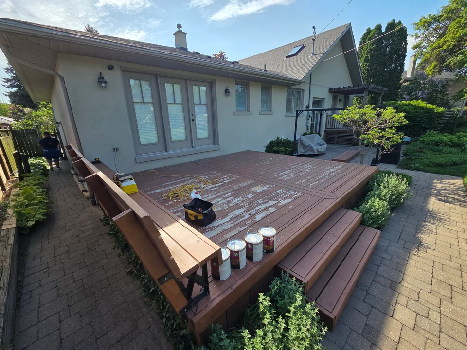 Deck staining in progress with tools and cans beside the steps