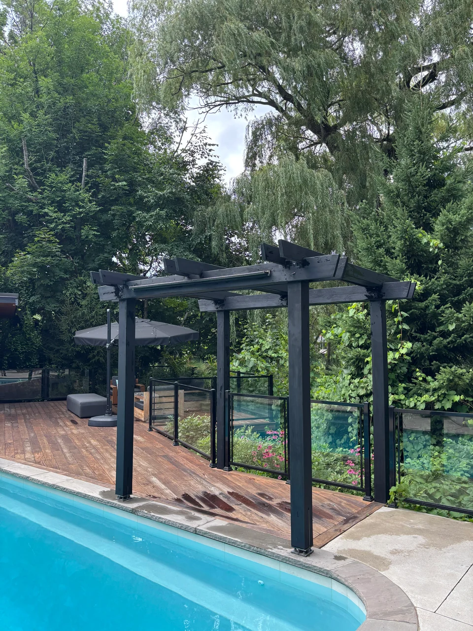 Angled view of a black pergola over the poolside wood deck