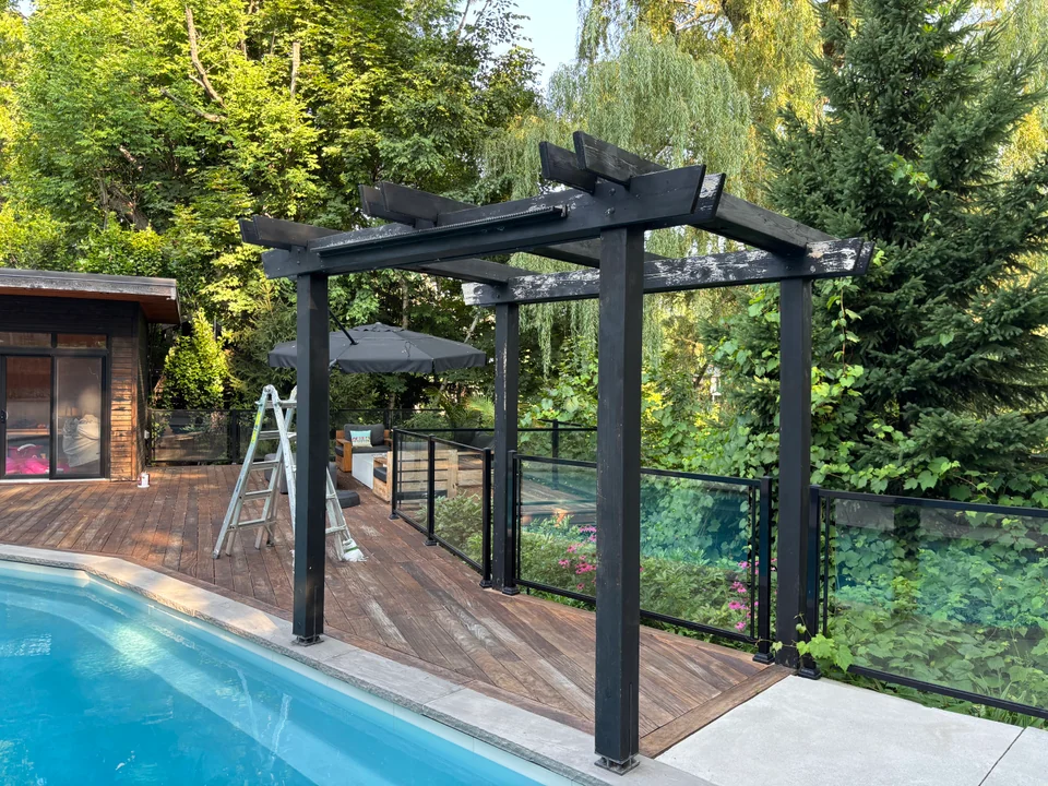 Poolside wood deck with black pergola beams and glass fence panels