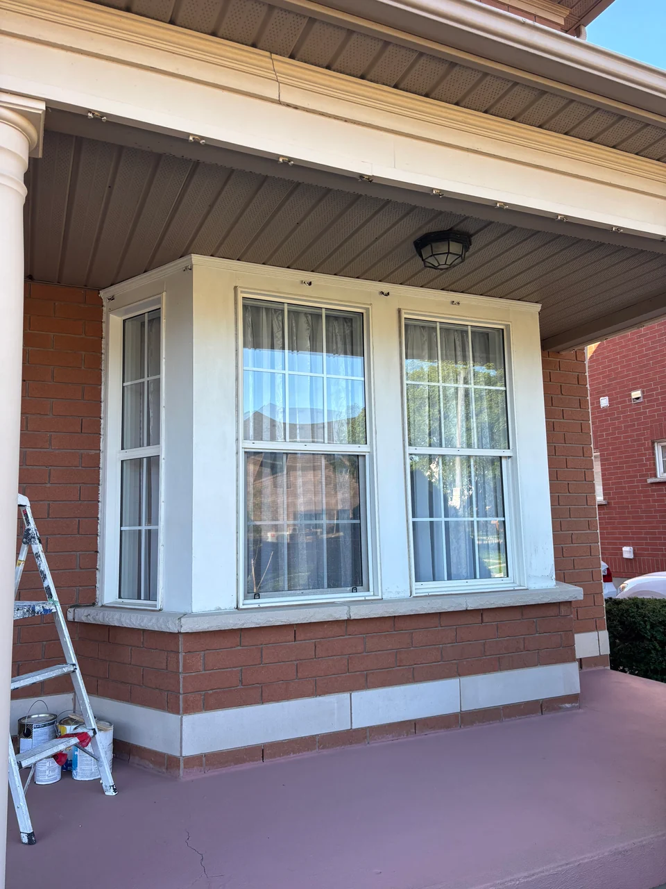 After: refreshed porch window trim with ladder beside the bay window