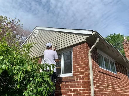 Painter working on green siding above a red brick exterior wall