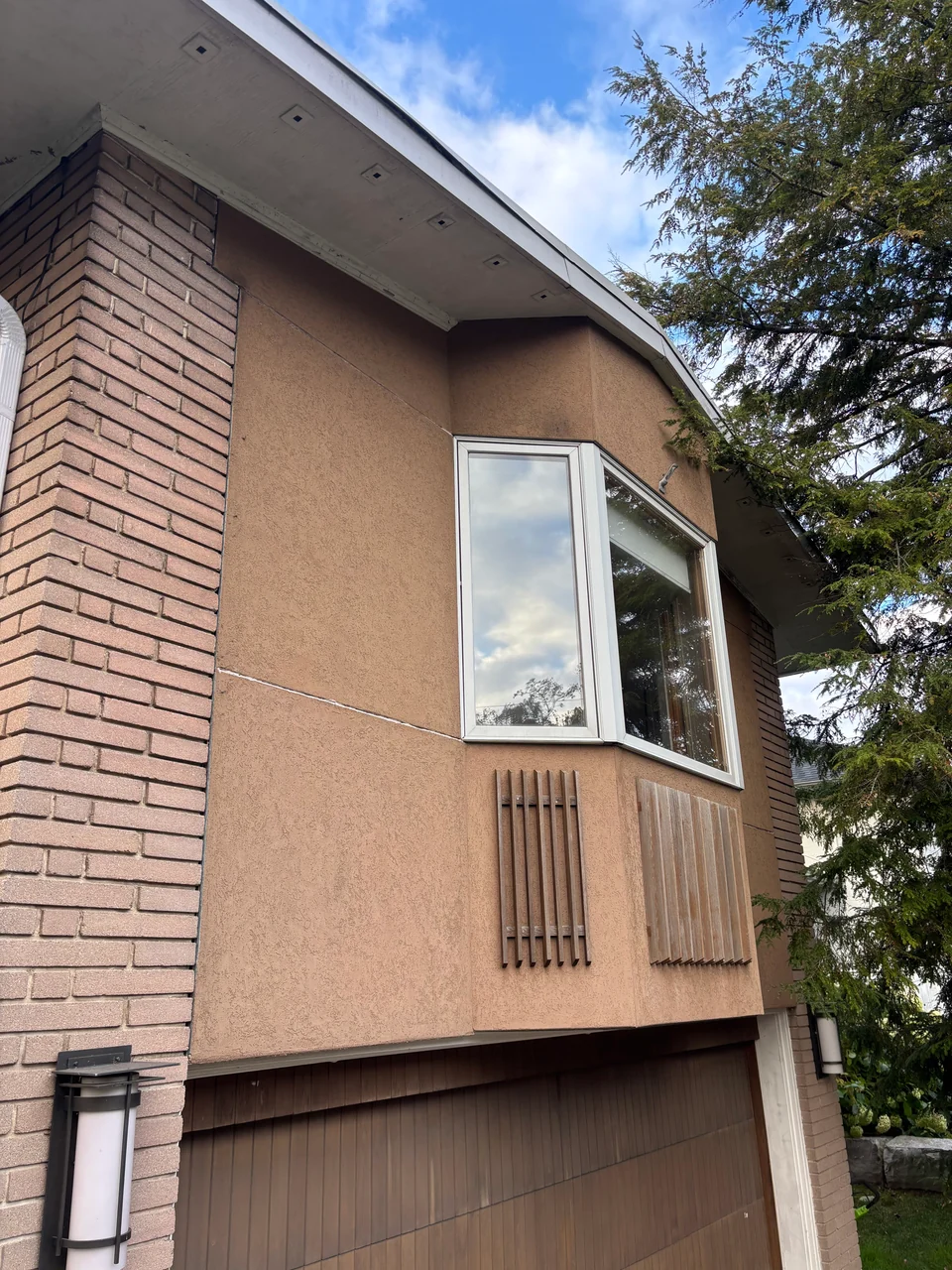 Tan stucco wall and projecting window beside exterior brickwork