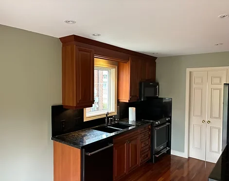 Finished pale kitchen walls beside wood cabinets and a black countertop