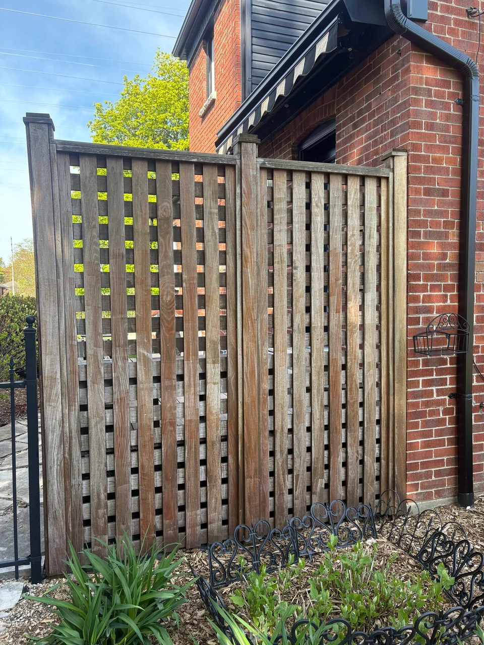 Before: weathered lattice privacy fence beside a brick house