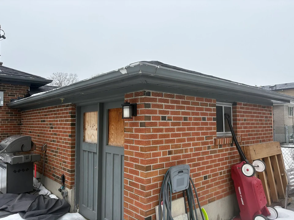 Before: grey garage fascia and trim beside exterior brickwork